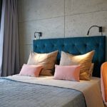 Punktowe oświetlenie w sypialni, w czarnym kolorze i minimalistycznym stylu, jest równie ważne co lampy sufitowe. Miękkość tkanin kontrastuje z surowością betonu na ścianie. Projekt sypialni - Hanna Pietras Pracownia Architektoniczna.