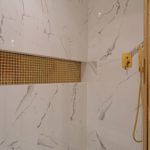 Projekt małej łazienki zakłada połączenie płytek imitujących marmur z bateriami w kolorze złotym. Projekt kawalerki - Studio Architektownia.